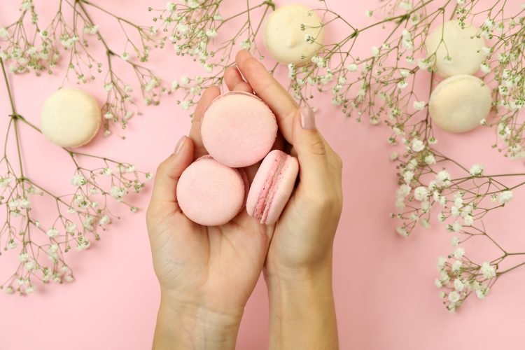 female-hands-hold-macaroons-on-pink-background-with-macaroons-and-flowers.jpg